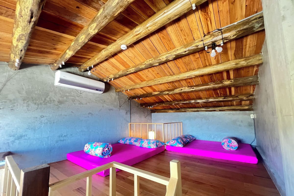A cozy attic bedroom with exposed wooden beams, a sloped ceiling, and a built-in bench with colorful cushions.