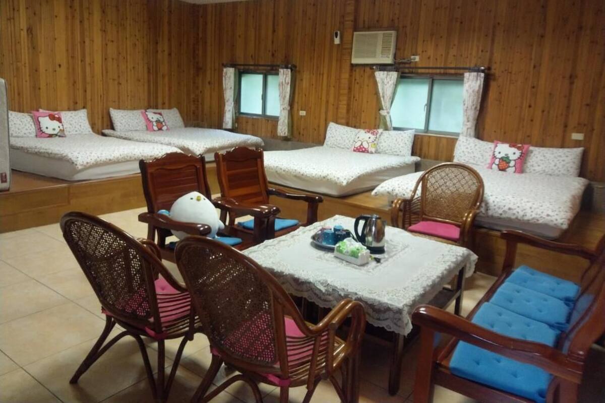 Een kamer met houten wanden, twee bedden met Hello Kitty kussens, een tafel met een theeservies en rieten stoelen met blauwe kussens.