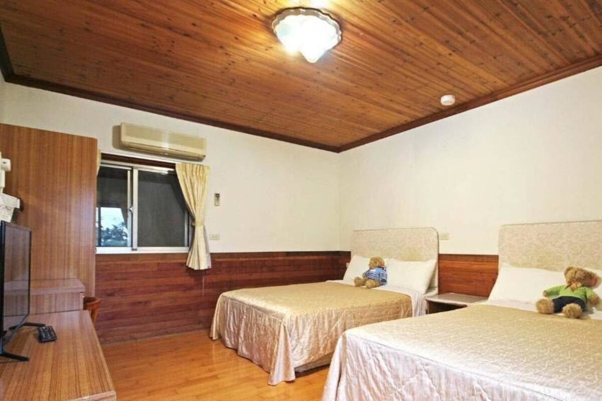 Een kamer met twee bedden, een houten plafond en een raam met gordijnen.