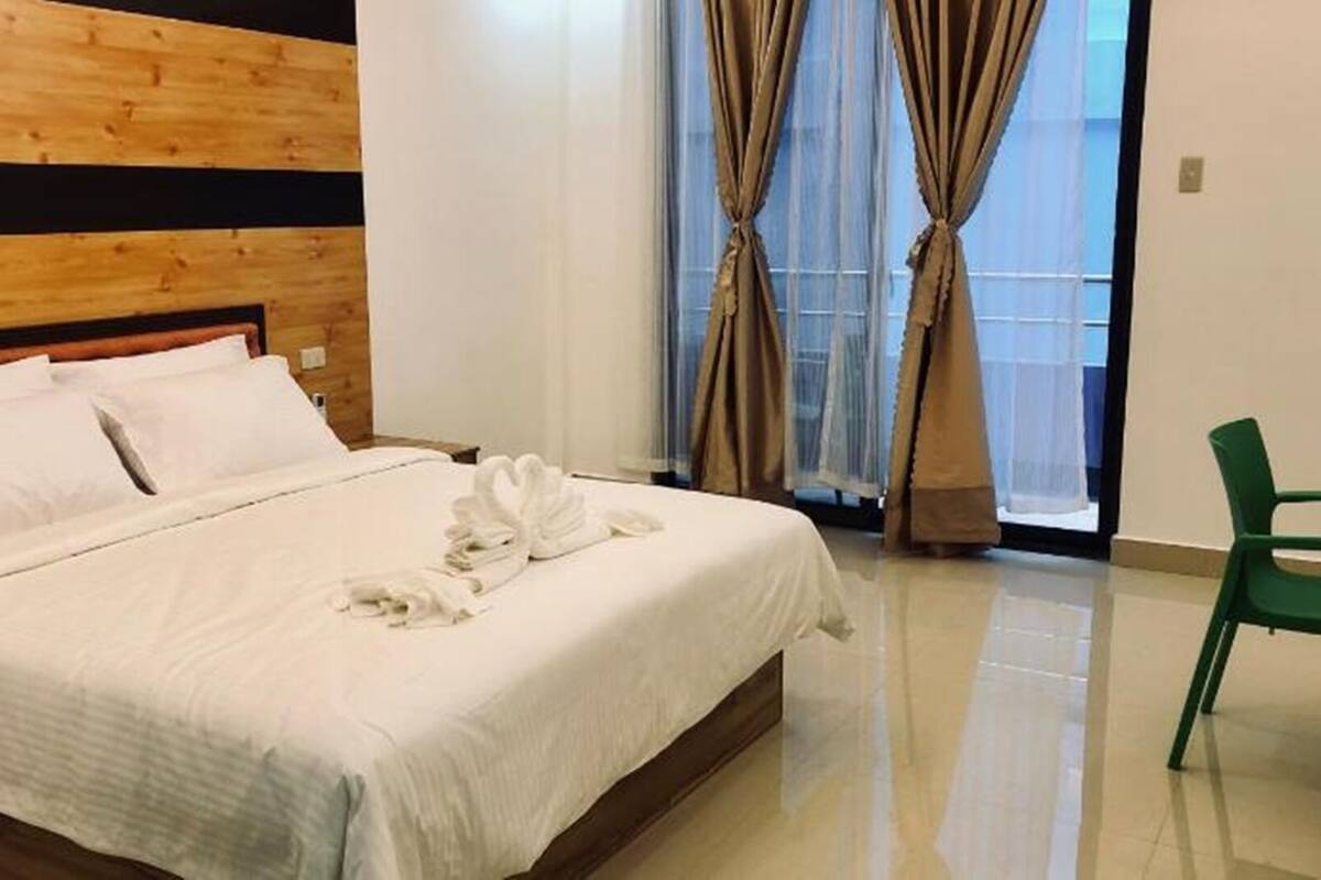 Ein Hotelzimmer mit einem hölzernen Kopfteil, einem ordentlich bezogenen Bett mit weißen Leinen und einem grünen Sessel.