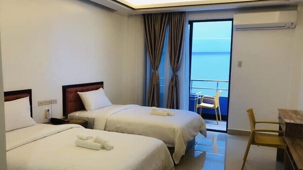 Habitación de hotel con dos camas, un escritorio, una silla y vista al mar.