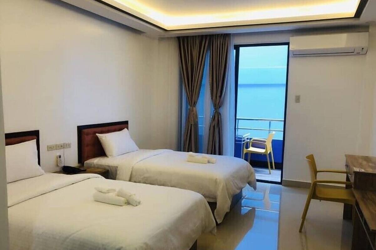 Ein Hotelzimmer mit zwei Betten, einem Schreibtisch, einem Stuhl und Meerblick.