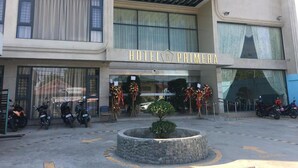 Hotel llamado "HOTEL PRIMERA" con fachada moderna, amplias ventanas y una jardinera de piedra en la entrada.
