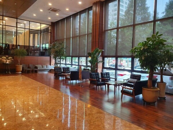 A spacious lobby with large windows, wooden flooring, and several seating areas.