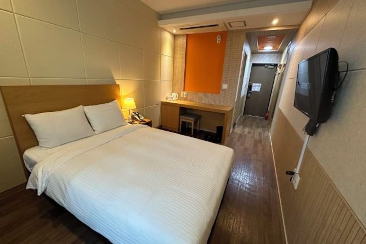 A hotel room with a large bed, a desk with a lamp, a television, and a small bathroom.