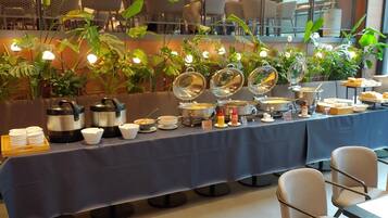 A buffet setup with various food items and condiments, surrounded by potted plants and seating areas.