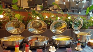 A buffet setup with various food items and condiments, surrounded by chairs and plants. - Hotel ICC (Daejeon)