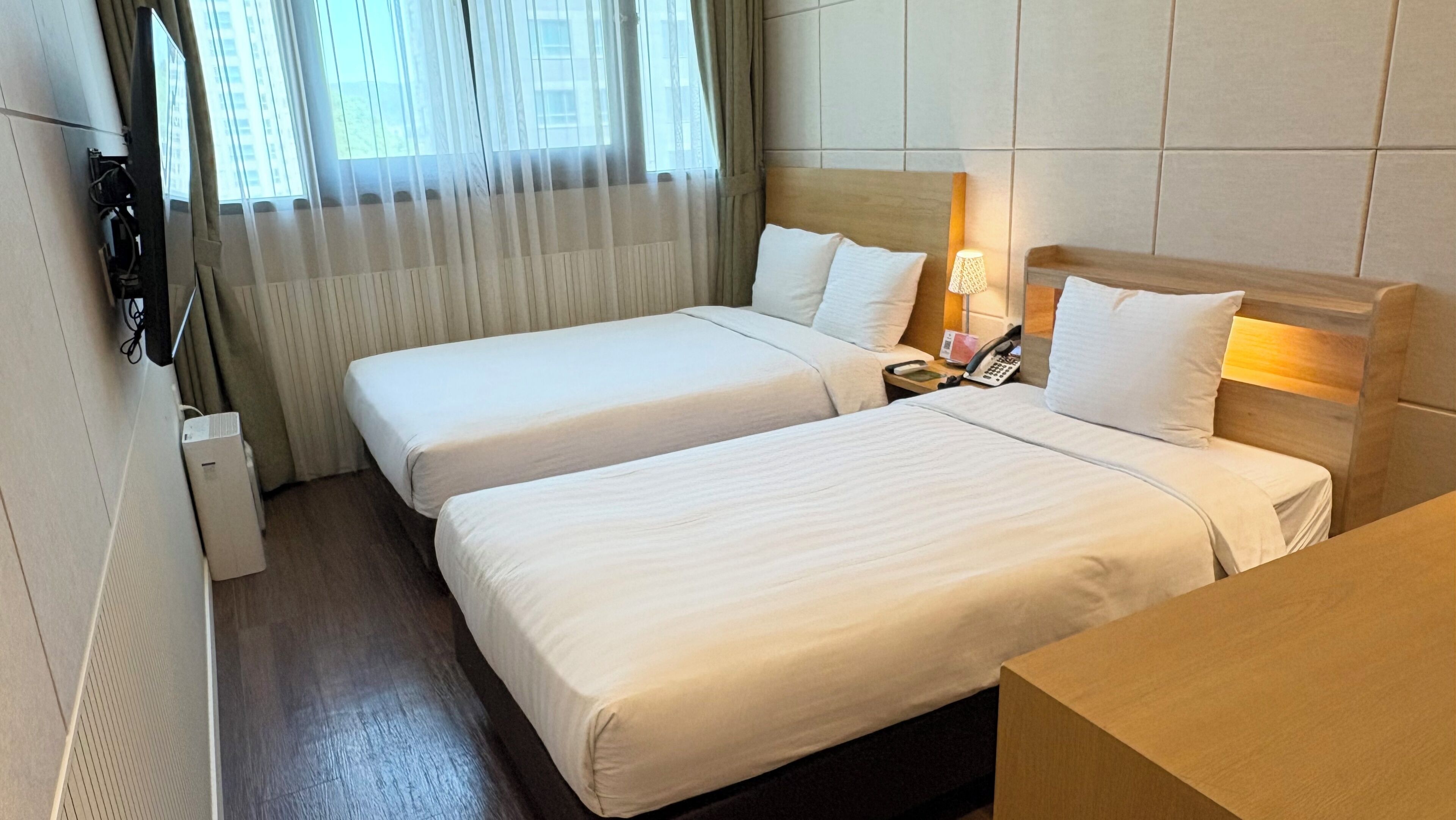 Une chambre d’hôtel avec deux lits, une table de chevet avec une lampe, un téléphone et un radiateur fixé au mur.