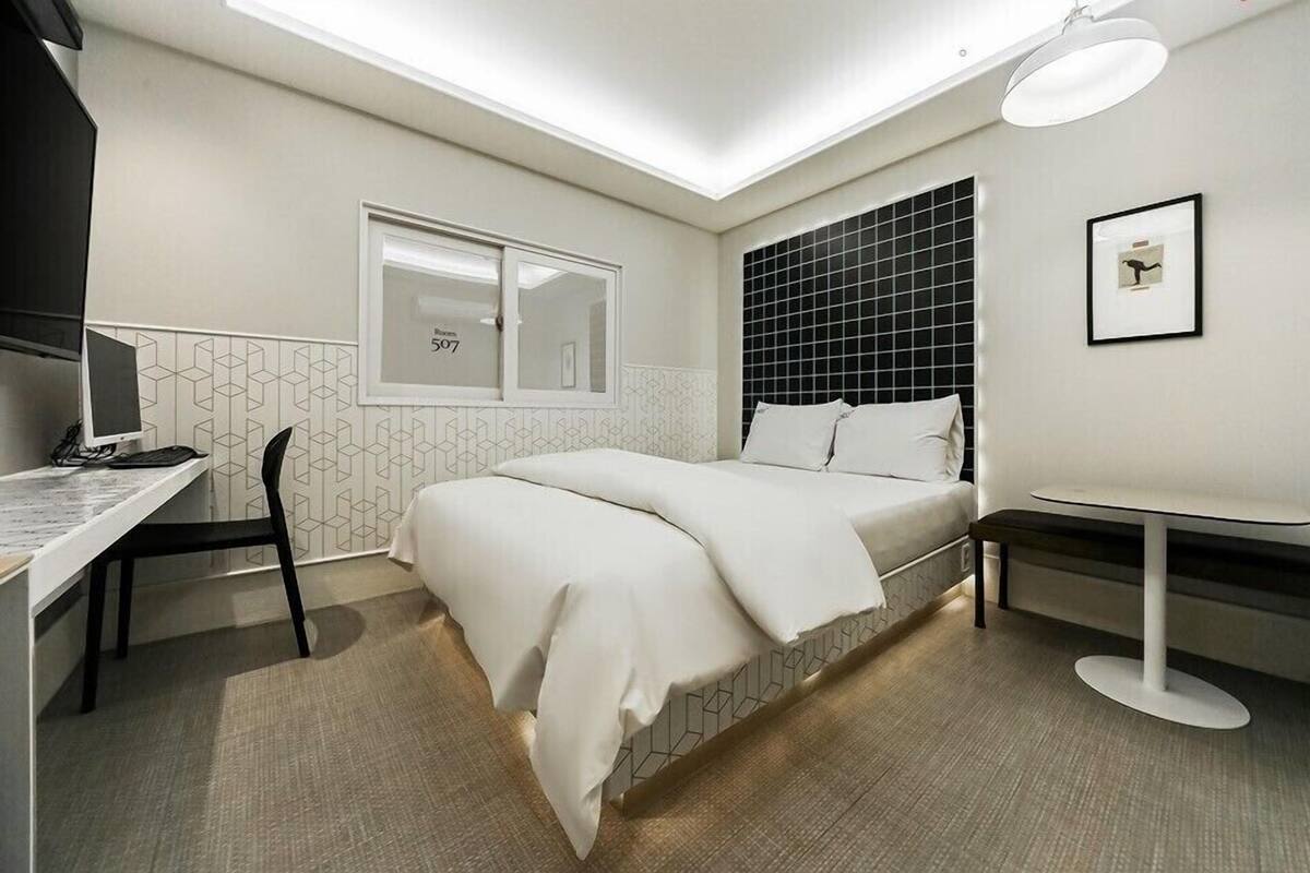 Una habitación de hotel moderna con una cama, un escritorio, una silla, una mesita pequeña y un cuadro en la pared.