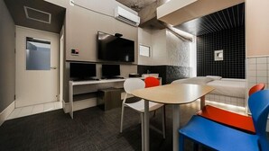 A compact hotel room with a kitchenette, a flat-screen TV, a small dining table, and a sofa.