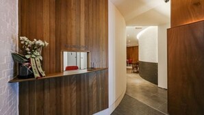 A reception desk with a wooden panel design, a white sign above it, and a vase with flowers on the left.
