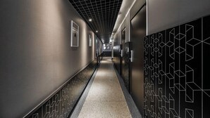 A modern hallway with a geometric patterned wall on the right, a tiled floor, and a grid ceiling.