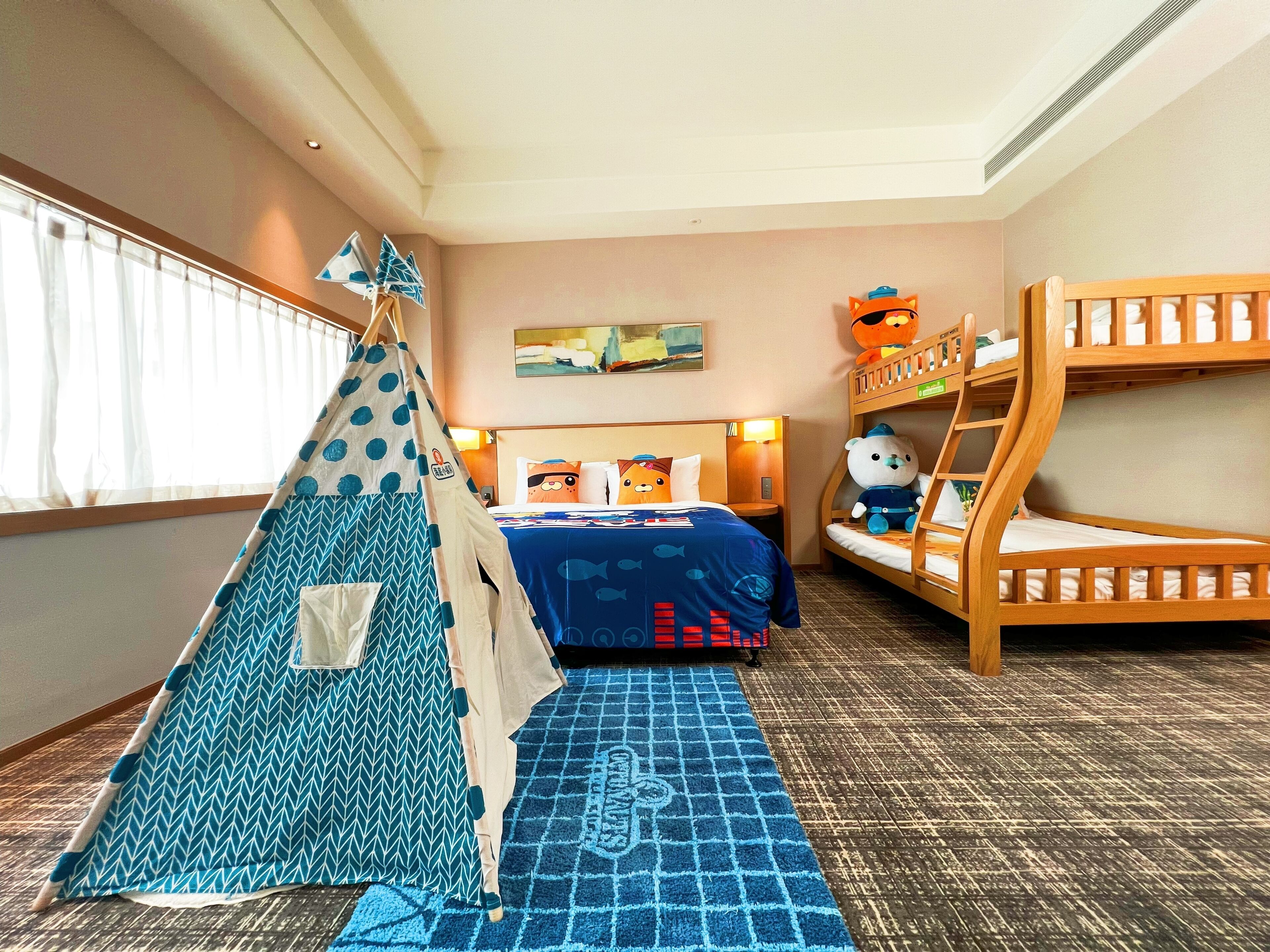 Una habitación de hotel con una litera, una tienda de campaña y una cama con edredón de motivos marinos azules.
