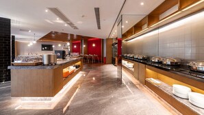 A modern breakfast area with a long counter, buffet-style food display, and seating area. - Xence Hotel (Xiamen)