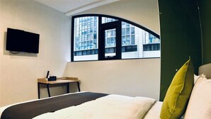 A hotel room with a bed, a desk, a TV, and a window with a view of buildings. - T.O Hotel Main Station (Taipei)