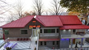 A hotel with a red roof, multiple floors, outdoor seating area, and a staircase leading to the entrance. - Dream Land Hotel (Murree)