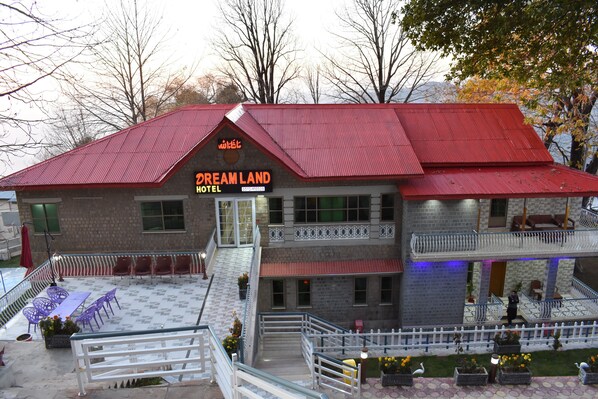 A hotel with a red roof, multiple floors, outdoor seating area, and a staircase leading to the entrance.
