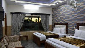 A hotel room with two beds, a sofa, a small table, and a window with curtains. - Dream Land Hotel (Murree)