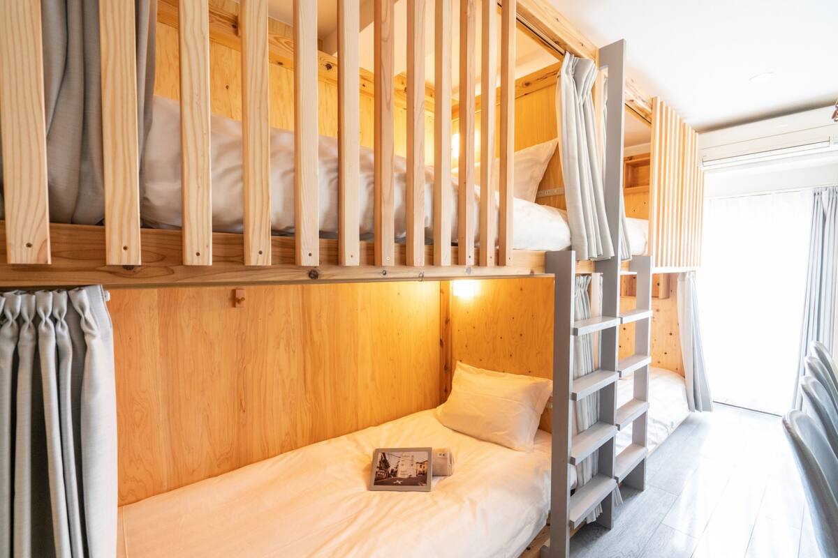 A bunk bed room with wooden walls, a small bedside table, and a window with curtains.