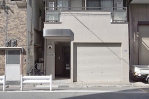 A building with a closed garage door, a small entrance with a bicycle, and a bench outside. - ZAITO Tokyo Kinshicho Economy Inn (Tokyo)