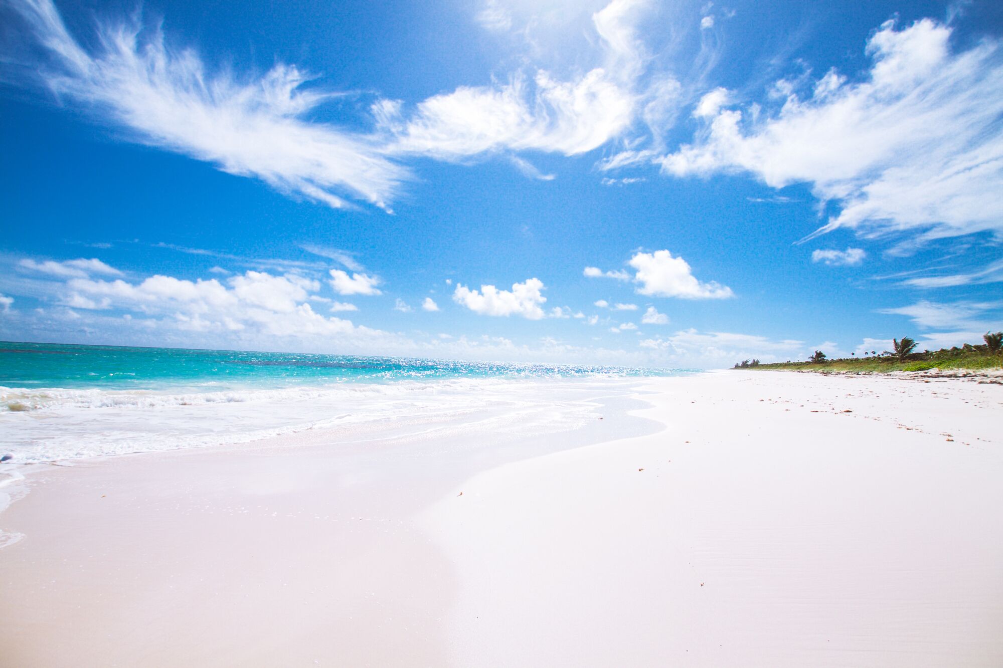 A wide sandy beach with a clear blue sky and ocean.