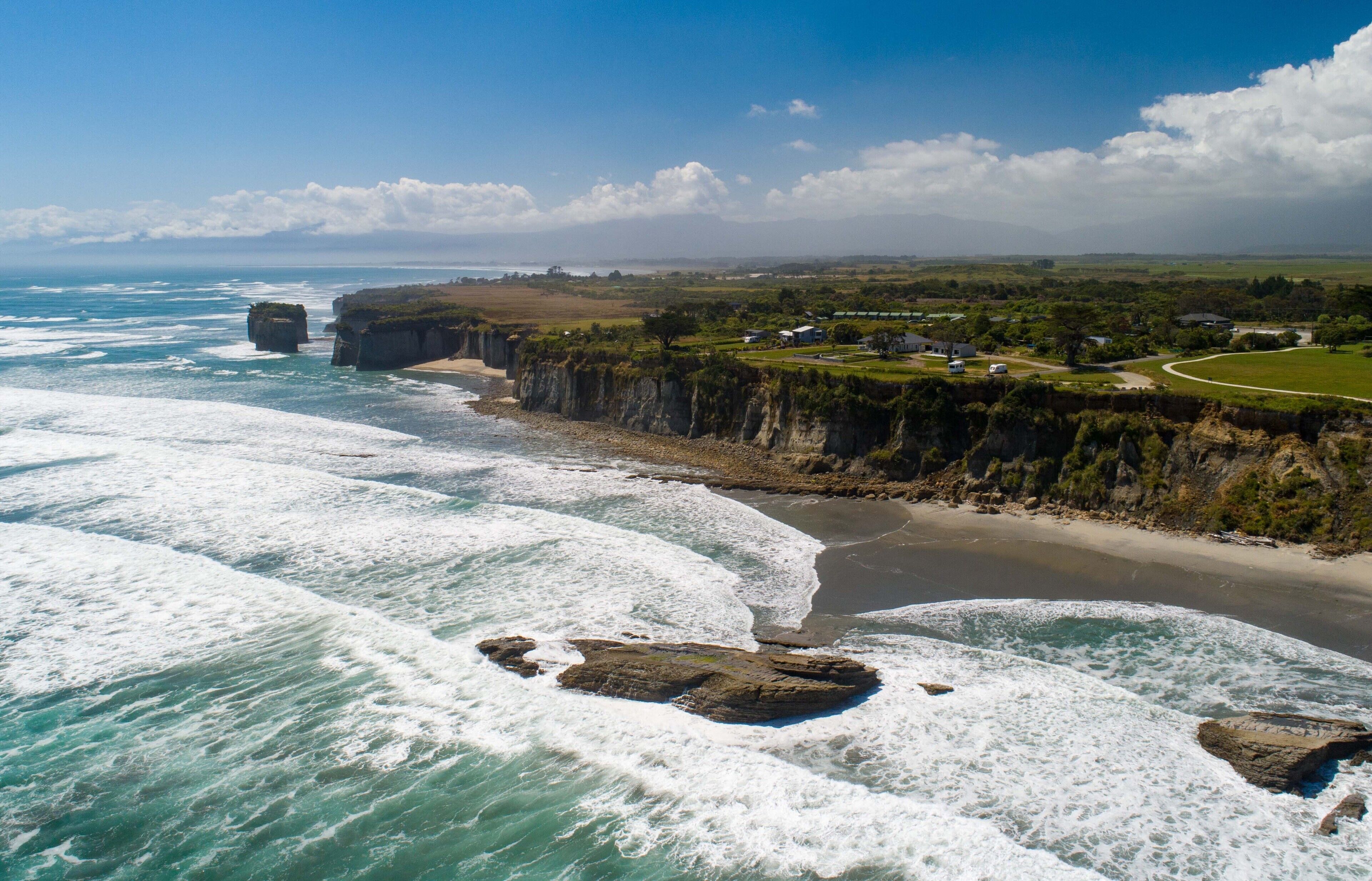 A coastal landscape with cliffs, a beach, and a road curving along the coastline.
