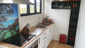 Une cuisine compacte équipée d’une cuisinière, d’un évier et d’une fenêtre donnant sur un espace verdoyant.
