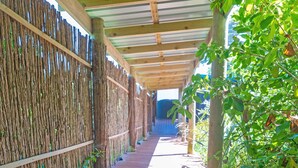Une terrasse en bois, avec une clôture en bambou d’un côté et un espace abrité doté d’un toit en métal.
