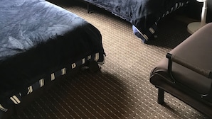 Quarto com duas camas, uma mesa de cabeceira com abajur, uma cadeira e luminária pendente.