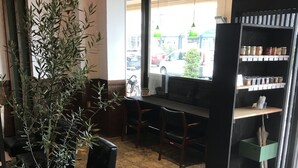 Interior de café com uma grande planta em vaso, móveis de madeira e vista para a rua pela janela.