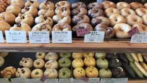Vitrine de uma padaria exibindo diversos produtos de panificação, incluindo bagels e doces, cada um com etiqueta de preço.