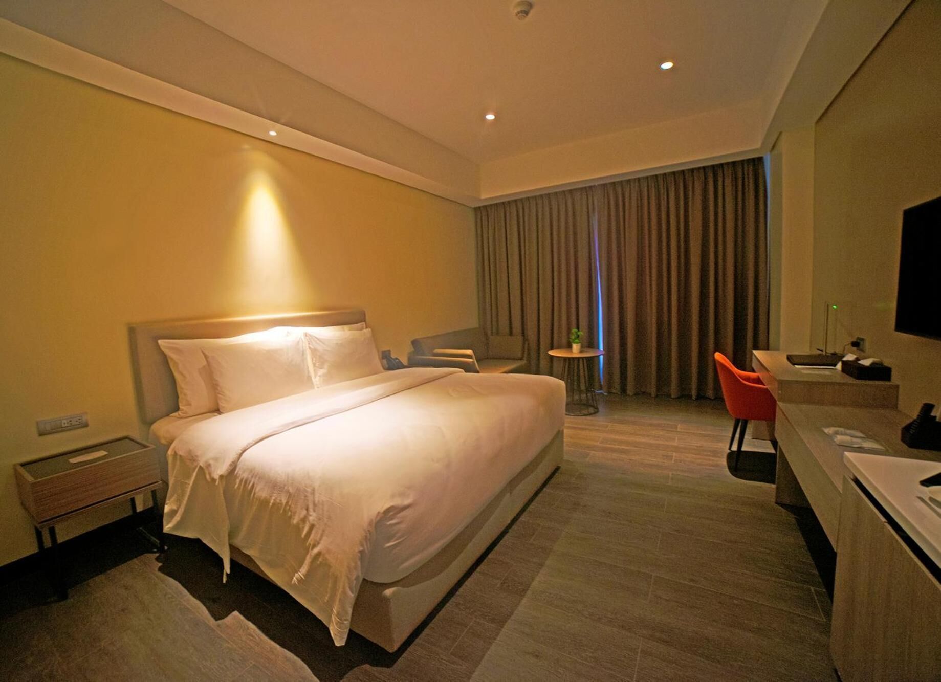Ein Hotelzimmer mit einem großen Bett, einem Schreibtisch, einem Sessel, einem kleinen Tisch und einem Fernseher.