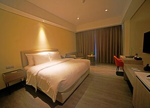 A hotel room with a large bed, a desk, a chair, a small table, and a TV. - Acacia Hotel Davao (Davao)