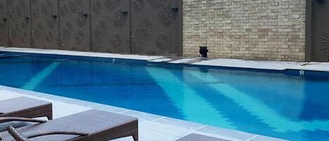A swimming pool with lounge chairs and a stone wall with floral carvings.