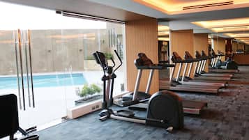 Un gimnasio con cintas de correr y una máquina elíptica, amplias ventanas y vistas a una piscina.