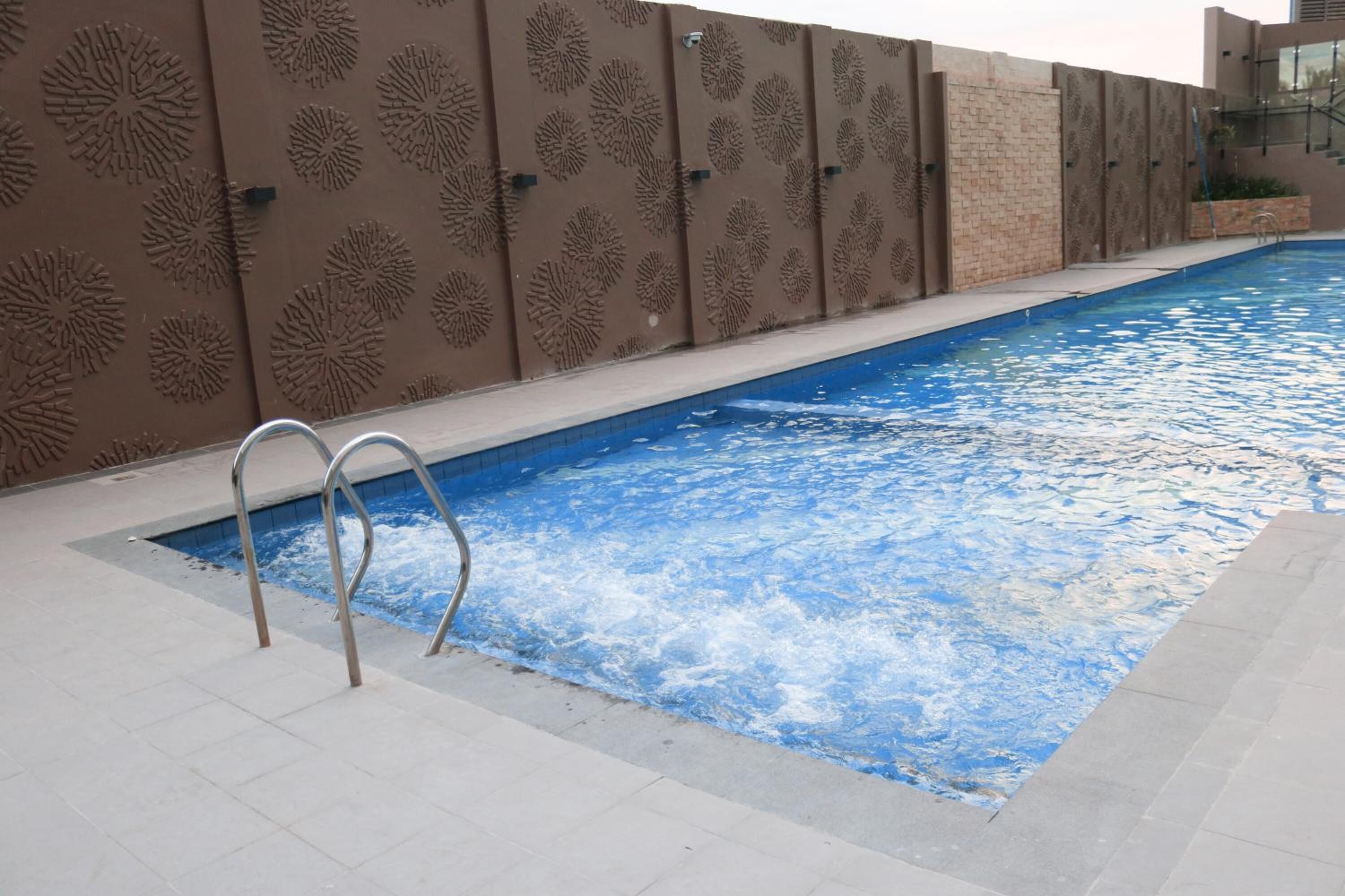 A swimming pool with a metal ladder, surrounded by a patterned wall.