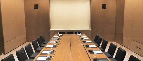 A conference room with a long table, black chairs, nameplates, and a projector screen.