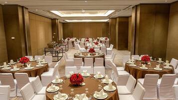 Un salón de banquetes con mesas redondas dispuestas para cenar, sillas blancas y centros de mesa florales rojos.