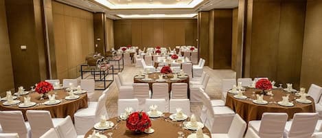 Un salón de banquetes con mesas redondas dispuestas para cenar, sillas blancas y centros de mesa florales rojos.