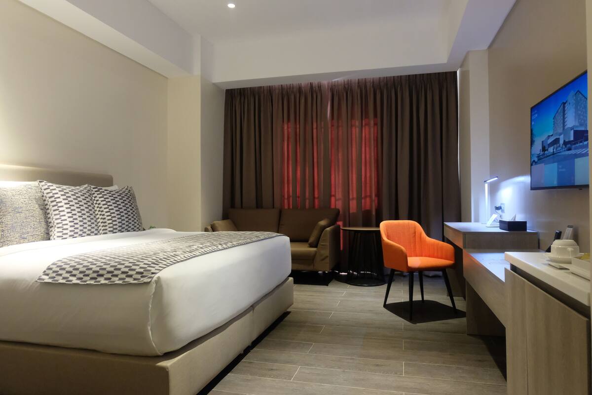 A hotel room with a large bed, a sofa, a desk, and a TV.