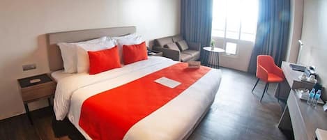 Ein Hotelzimmer mit einem großen Bett, einem Schreibtisch, einem Sessel, einer Couch und einem kleinen Tisch.