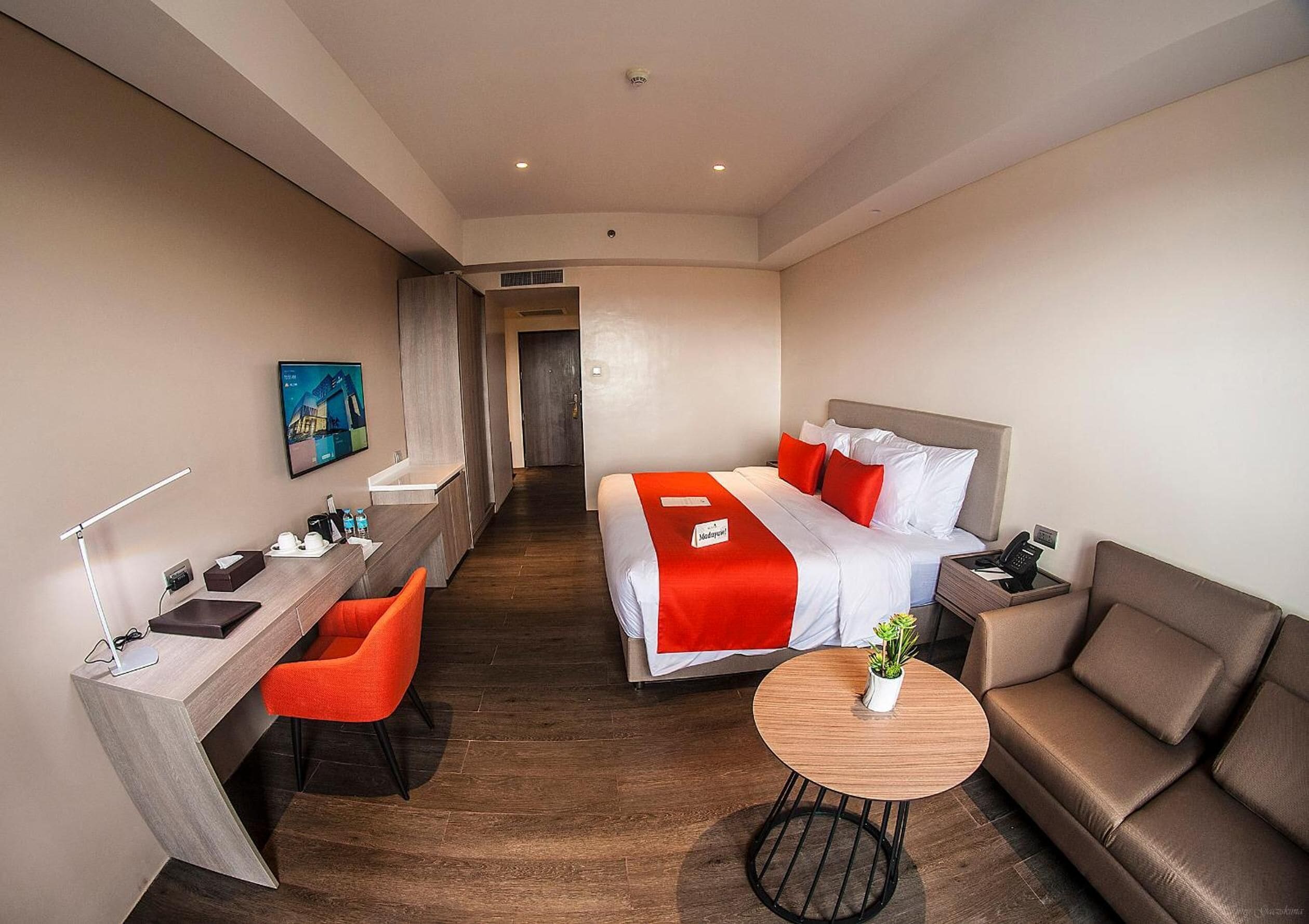 Hotelkamer met een bed, een bureau, een stoel, een bank en een kleintje tafeltje met een plant.