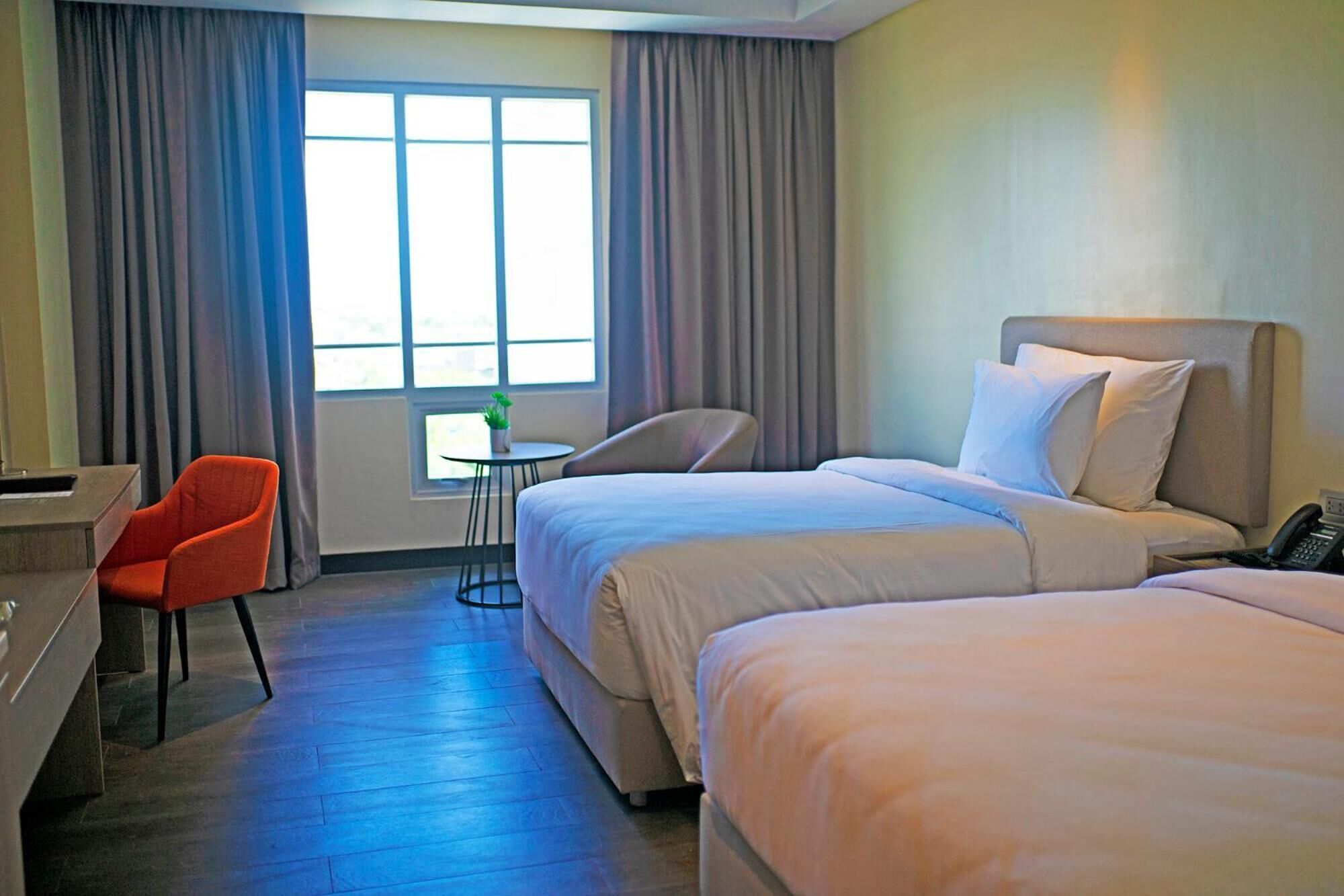 A hotel room with two beds, a desk, a chair, and a small table with a plant.