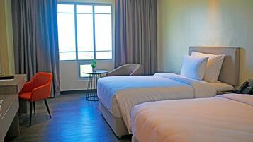 A hotel room with two beds, a desk, a chair, and a small table with a plant.