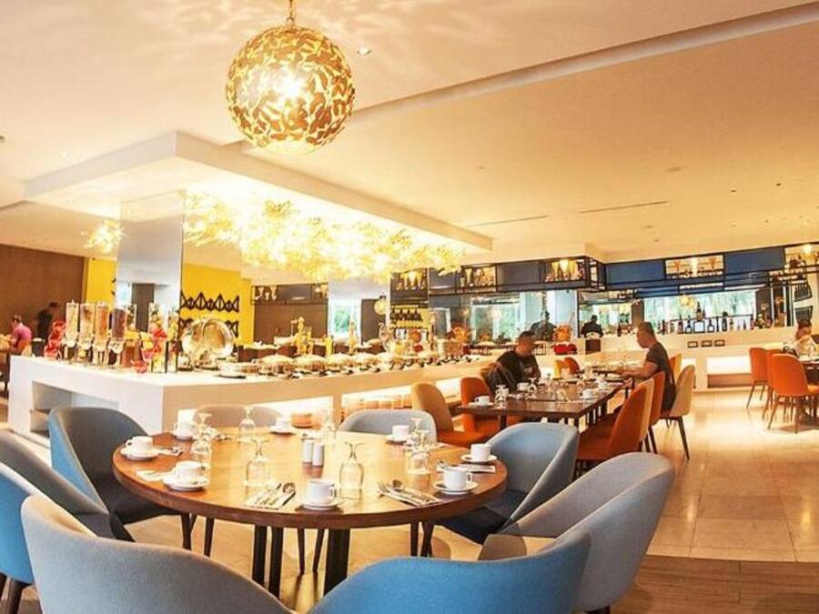 A modern restaurant with round tables and blue chairs, a bar area, and a visible kitchen in the background.