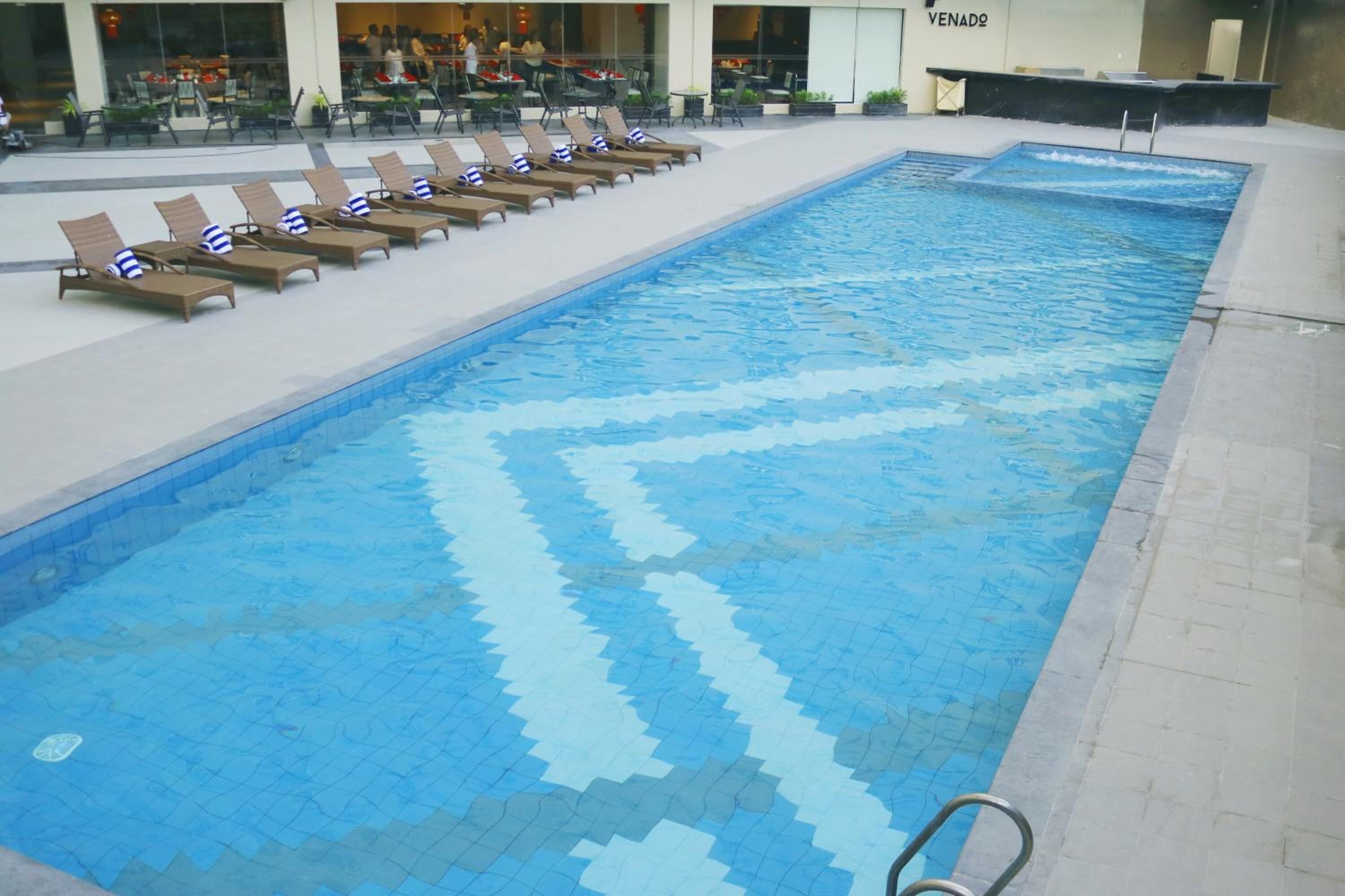 A swimming pool with a geometric tile pattern, surrounded by lounge chairs with blue and white striped pillows.