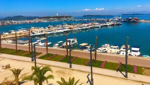 Un port de plaisance où sont amarrés de nombreux bateaux, un ciel bleu azur et une vue lointaine sur une côte bordée de montagnes.