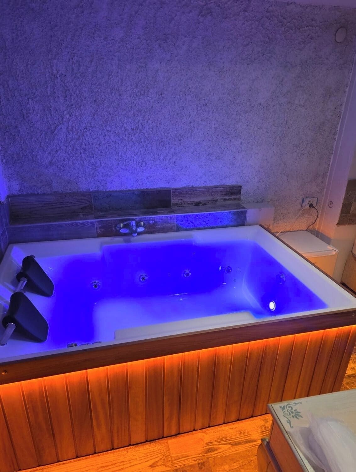 Un jacuzzi rectangular con estructura de madera y luz azul.