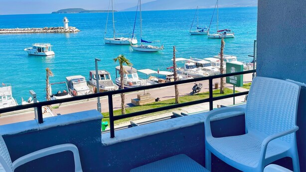 Un balcon agrémenté de chaises en osier blanc et d’une petite table, d’où l’on peut admirer un port de plaisance avec des voiliers et un phare.