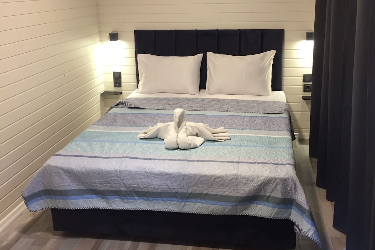 A hotel room with a bed, a wall-mounted air conditioner, and a wooden ceiling.